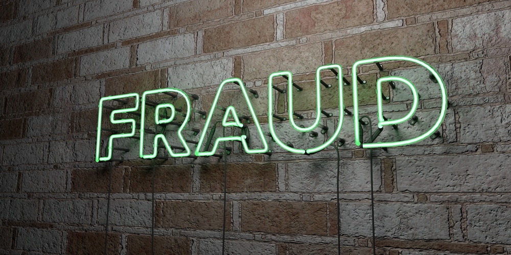 FRAUD neon sign on a brick wall