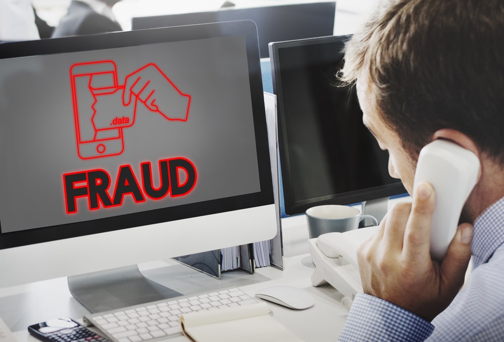 Man on phone at desk with FRAUD on screen