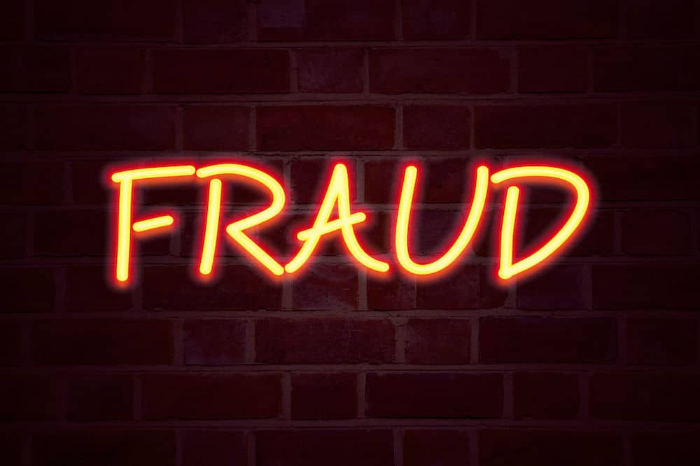 Neon sign reading FRAUD over brick wall