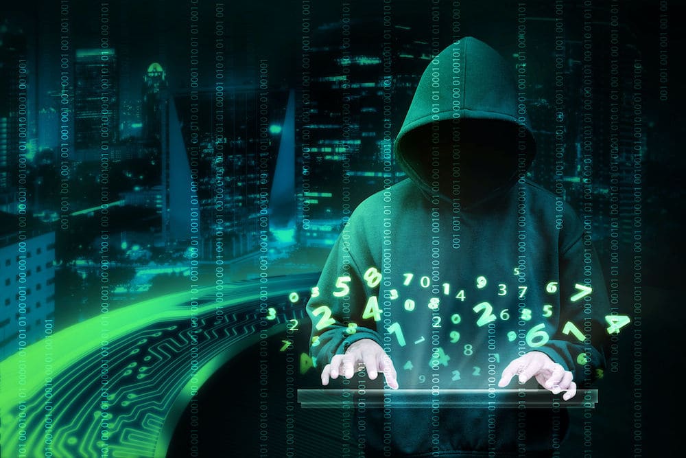 Hooded figure amidst lines of binary code and using a keyboard 