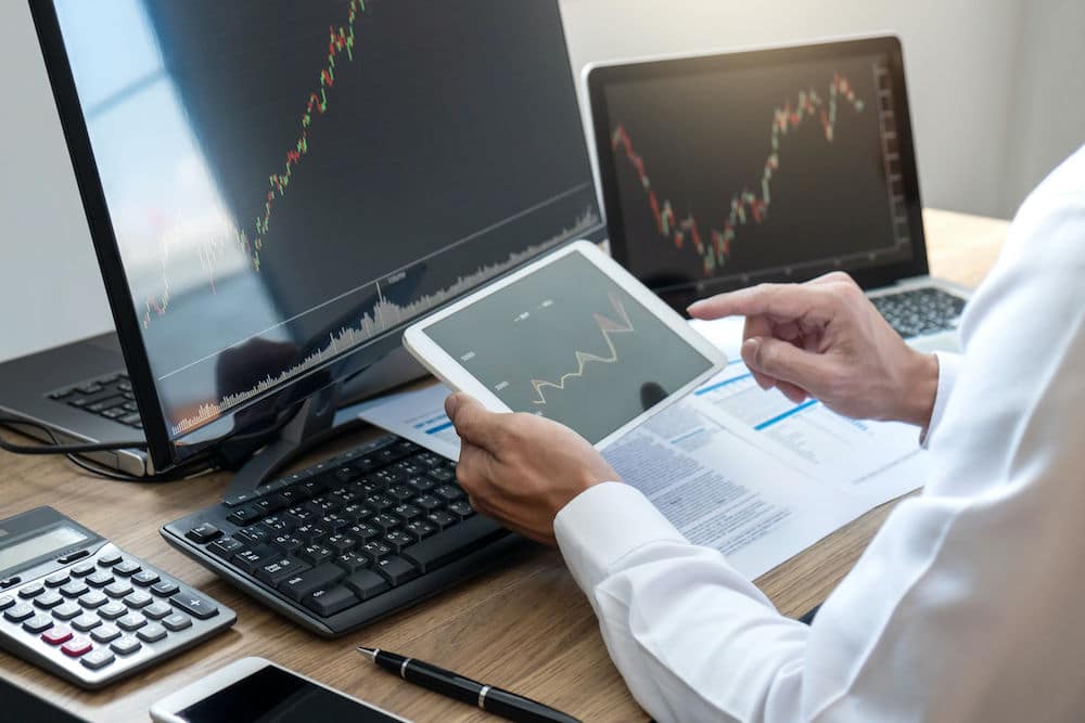 Man at Desk using Tablet, Laptop and PC to look at Forex Price Graphs