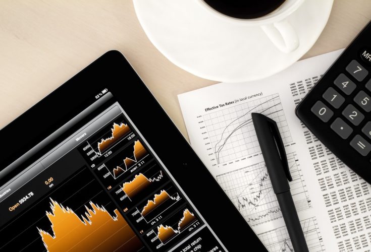 Stock image of a tablet with price graphs, pen, calculator and coffee mug