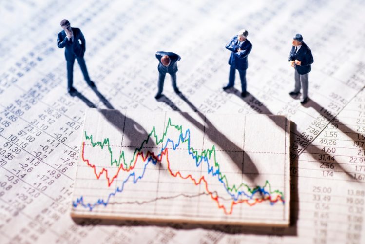 Four toy men looking at a Stock Market Graph on a wooden block