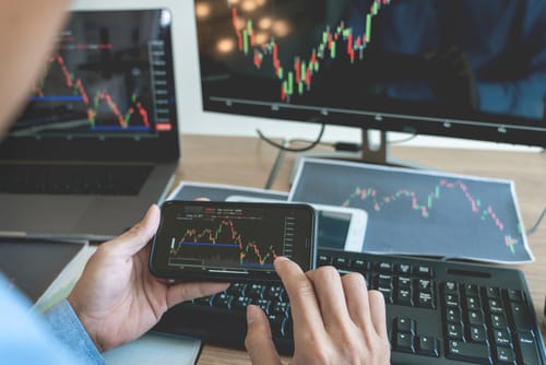 Man looking at stock market graphs on phone, laptop and PC