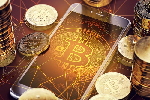 Physical rendition of Bitcoins piled around a phone with Bitcoin logo 