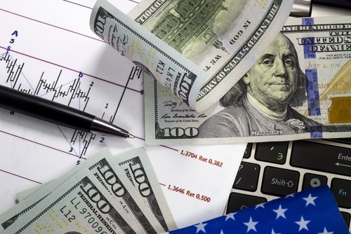 US Dollars on top of a keyboard, alongside a stock market price chart