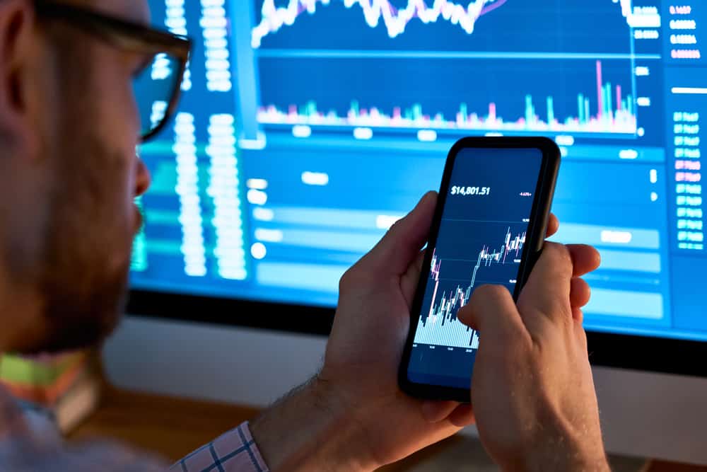 Man Looking On Phone at Stock Market Graph